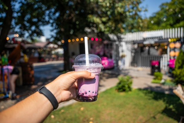 Hand Holding Bubble Tea Against Urban Market Backdrop