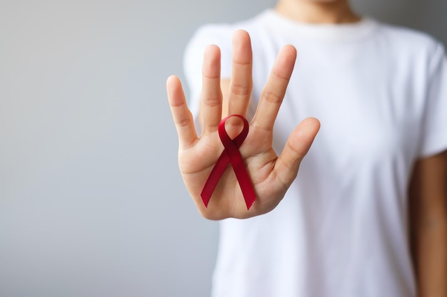 Hand holding Burgundy Red Ribbon for March multiple myeloma Cancer and December World Aids Day Awareness month. Healthcare and world cancer day concept