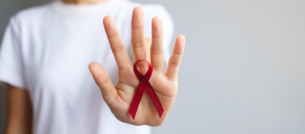 Hand holding Burgundy Red Ribbon for March multiple myeloma Cancer and December World Aids Day Awareness month. Healthcare and world cancer day concept