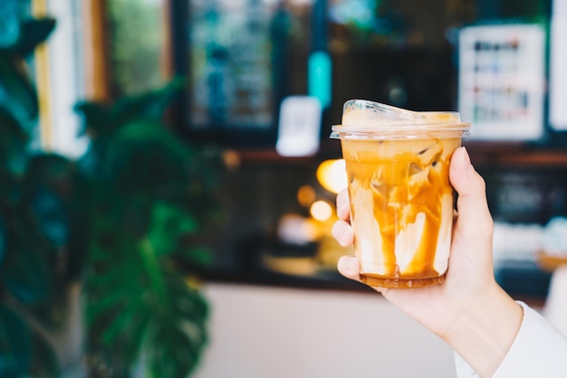 hand holding caramel macchiato coffee in takeaway glass