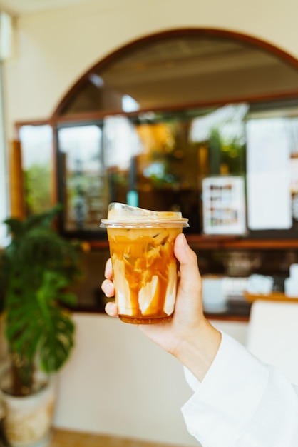 hand holding caramel macchiato coffee in takeaway glass