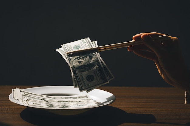 Hand Holding the chopsticks pick up the banknotes on the plate The concept for corruption bribery and The inflation rate shows that the expenditures are higher each day Higher cost of living