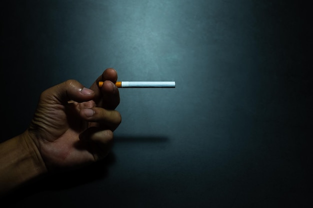 Hand holding a cigarette in the dark darkness against dark blue background