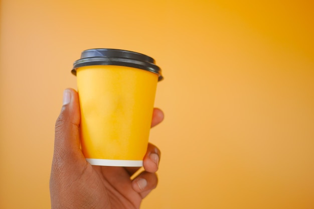 Hand holding coffee cup against yellow background perfect for cafe or lifestyle concepts