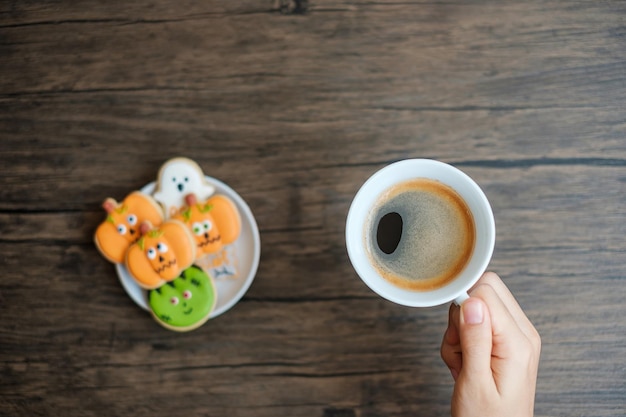 Hand holding coffee cup during eating funny Halloween Cookies Happy Halloween day Trick or Threat Hello October fall autumn Traditional party and holiday concept