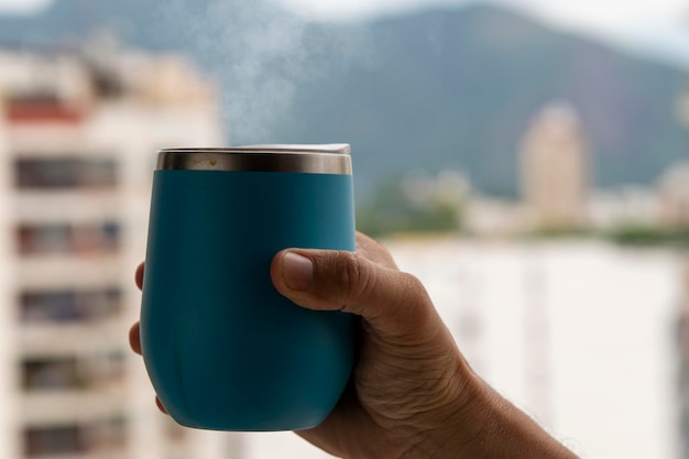 Hand holding a coffee mug coming out of smoke with urban environment background