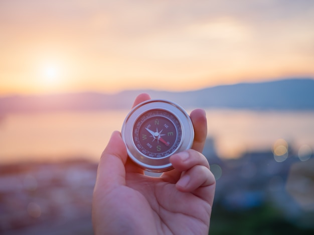 Hand holding compass with  mountain and sunset sky background.