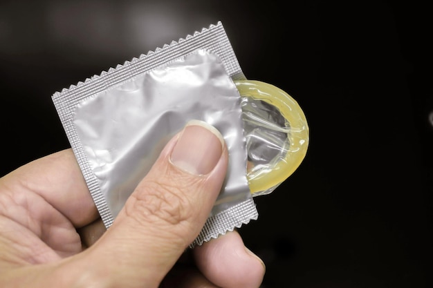 Hand holding a condom in a silver package are opened picking up on black background