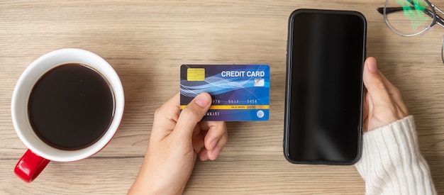 Hand holding credit card for online shopping on smartphone during drinking coffee. Merry Christmas eve, December, seasonal, Black Friday sale, New Year and holiday concept