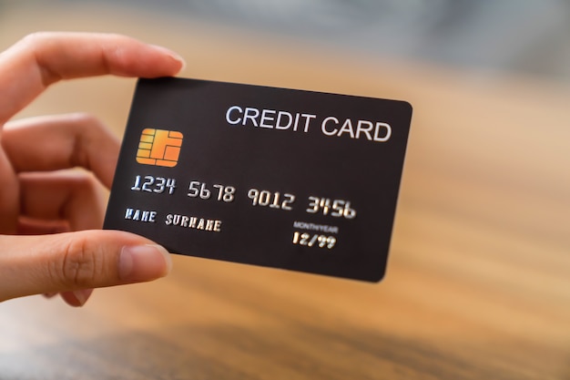 Hand holding credit card on wood table.