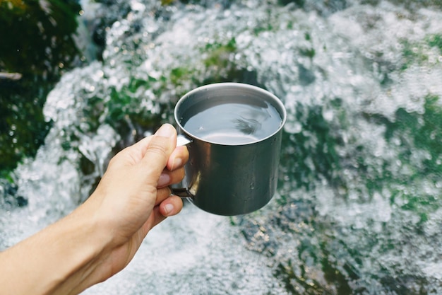 Hand holding cup with pure waterfall drinking water