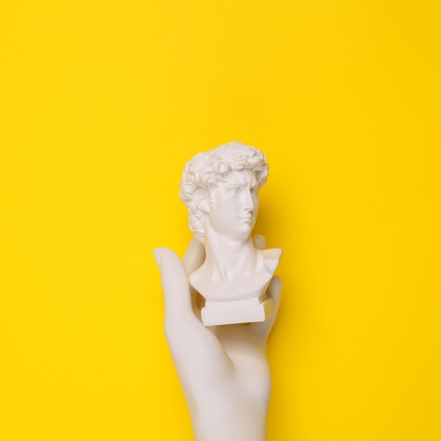 Hand holding David bust on yellow background Minimal still life