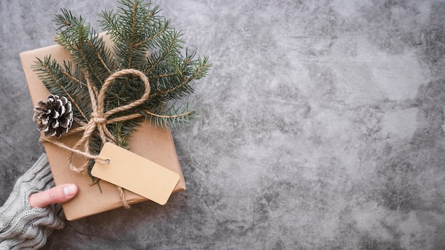 Hand holding decorated gift box with snag, label and fir twigs