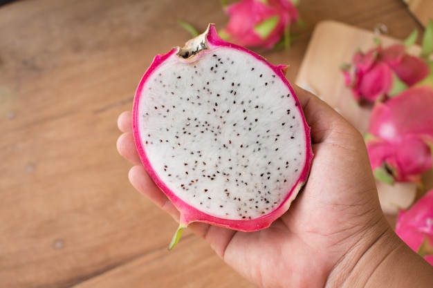 Hand holding Dragon fruits on wooden background, Sliced delicious dragon fruit on wooden background.