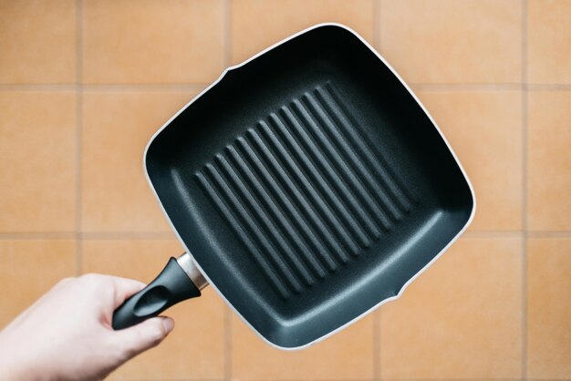 Hand holding empty non-stick square frying pan over kitchen floor background with copy space.