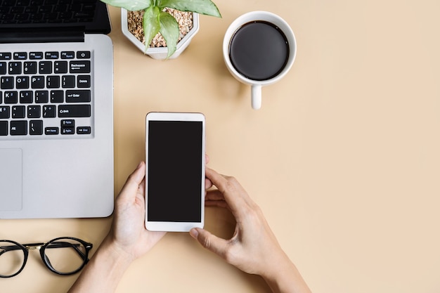 Hand holding empty screen Smart phone on business desk office with copy space, Top view