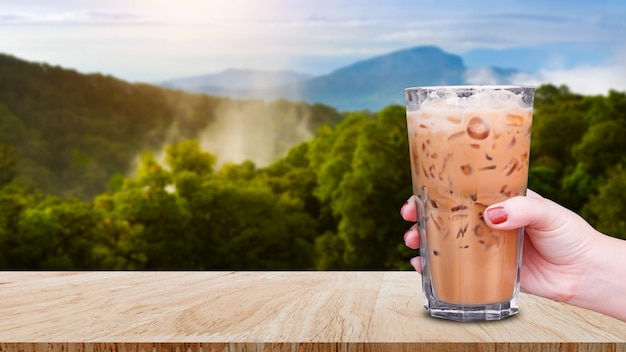 Hand holding the glass iced coffee on wooden table with landscape nature background Ice latte coffee