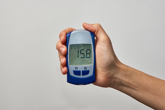 Hand holding glucometer with blood sugar test result. Womans hand showing sugar test, on white background with copy space