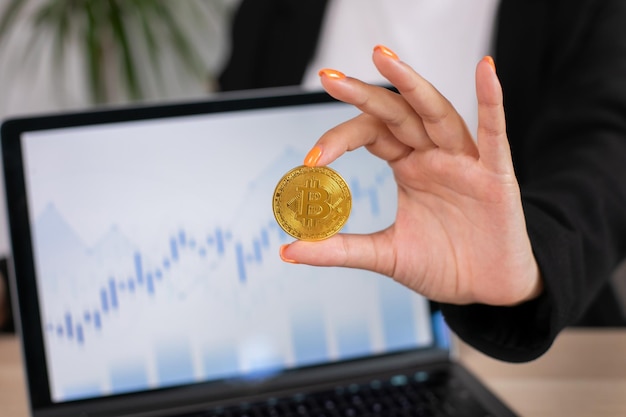 Hand holding gold bitcoin with blurred candlestick chart in the background