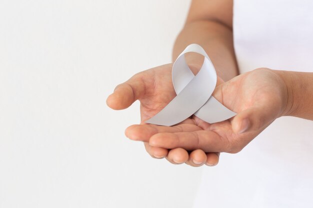 Hand holding Gray ribbon on white fabric background. Brain Cancer Awareness