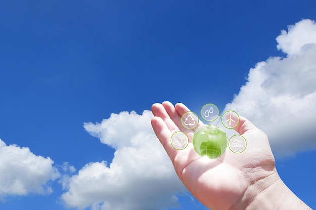 Hand holding green globe with eco energy icon on blue sky with white clouds background