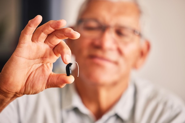 Hand holding hearing aid senior man and tech for ears health and wellness for retirement in nursing home Elderly person with disability audio or sound technology to listen in closeup at house