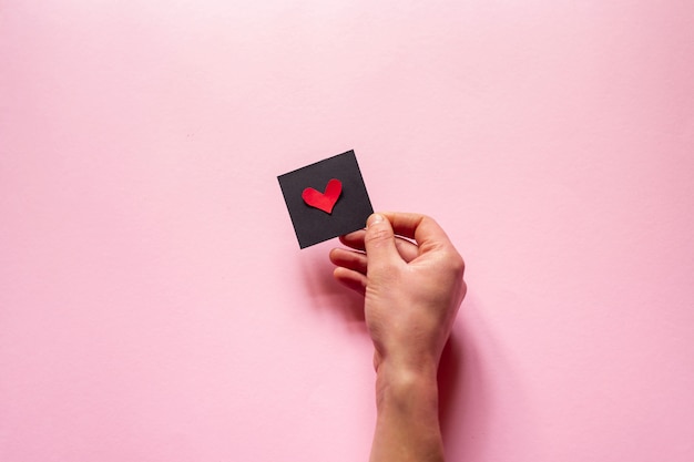 The hand  holding a heart  over pink wall, Valentine's Day. Flat Lay