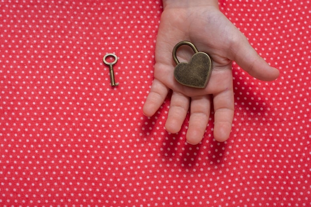 Hand holding a heart shaped lock and key on red background