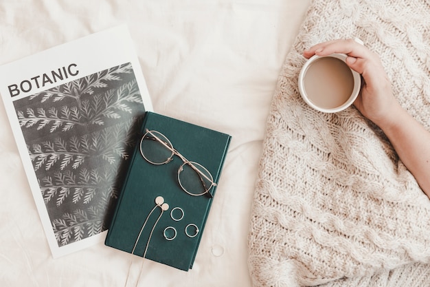 Hand holding hot drink near book eyeglasses and banner