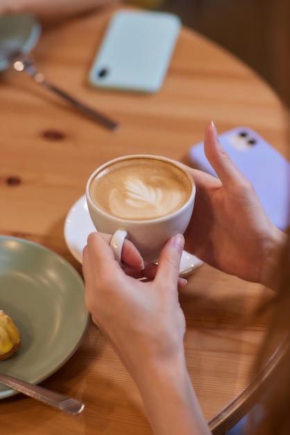 hand holding hot organic cocoa with foam froth art in black ceramic cup