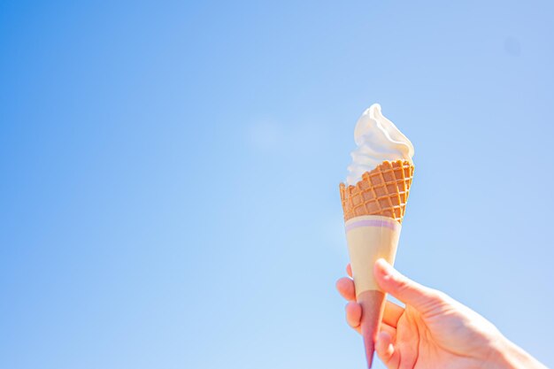 A hand holding an ice cream cone against a blue sky