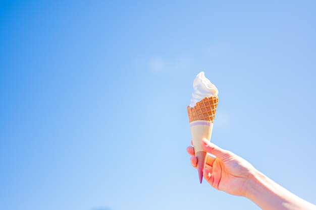 A hand holding an ice cream cone against a blue sky.