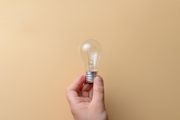 Hand holding an incandescent light bulb on a beige background