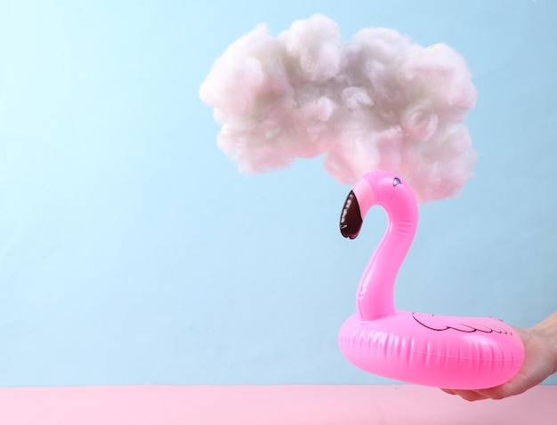 Hand holding Inflatable flamingo with cloud on pastel pink blue background Creative idea Summer fun Minimal concept Pastel color trend