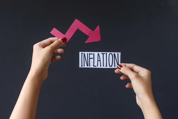 Hand holding Inflation text and graph chart arrow pointing down isolated on dark background.