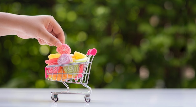 Hand holding jelly coated candy out of toy shopping cart