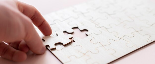 A hand holding a jigsaw piece and complete puzzle on the table