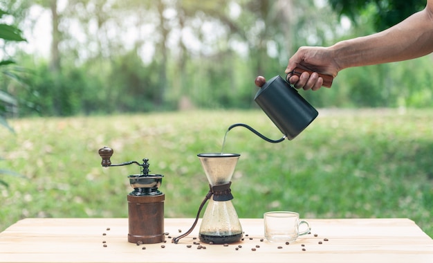 Hand holding a kettle and pouring hot water for make coffee with empty glass of coffee