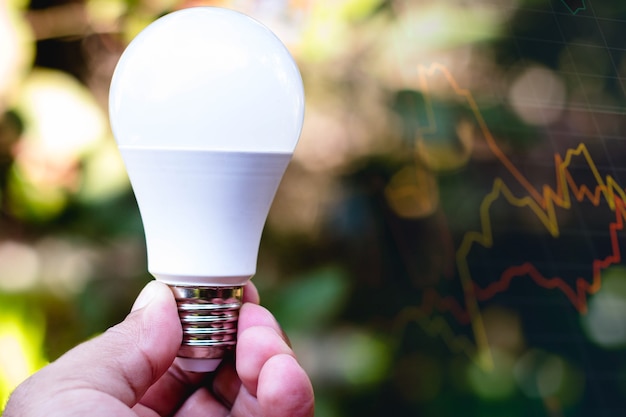 Hand holding a LED light bulb lightemitting diodes In the background graph of the stock exchange