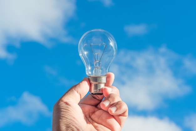 Hand holding light bulb and blue sky