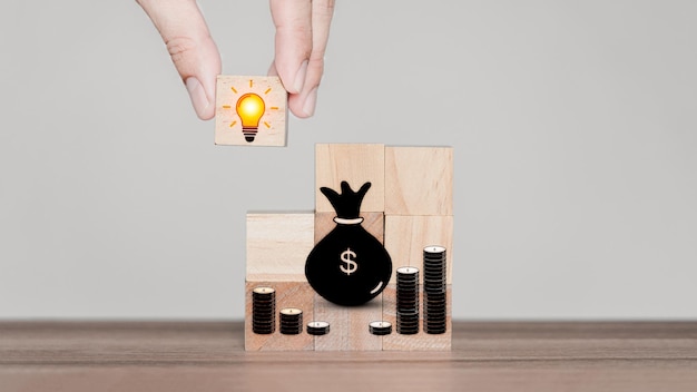 Hand holding light bulb creative icon on wooden cube block with money icon