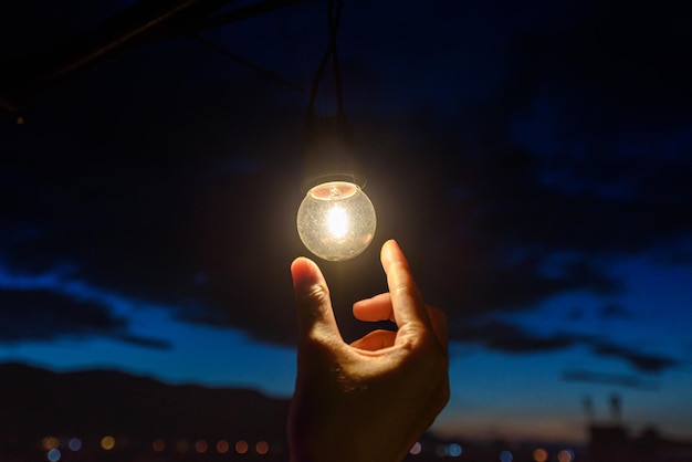 Hand holding light bulb in dark evening sky