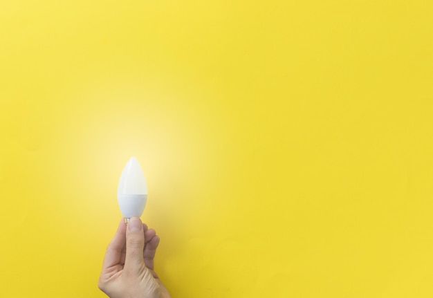 Hand holding lit white lightbulb on yellow background