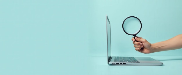 Photo hand holding magnifying glass over laptop on blue background