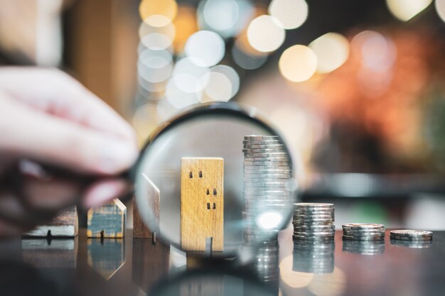 Hand holding magnifying glass and looking at house model