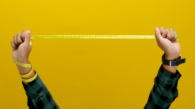 Photo hand holding a measuring tape against a yellow background