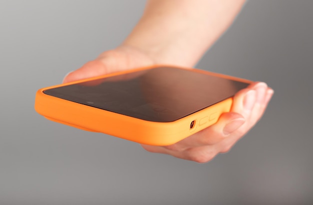 Hand holding mobile phone use smartphone cellphone in orange case close up