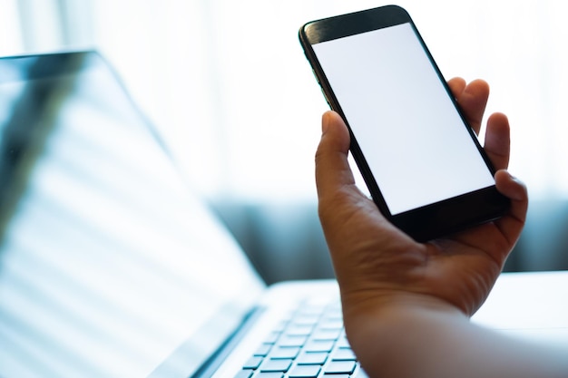 Hand holding a mobile phone with white blank screen over the laptop