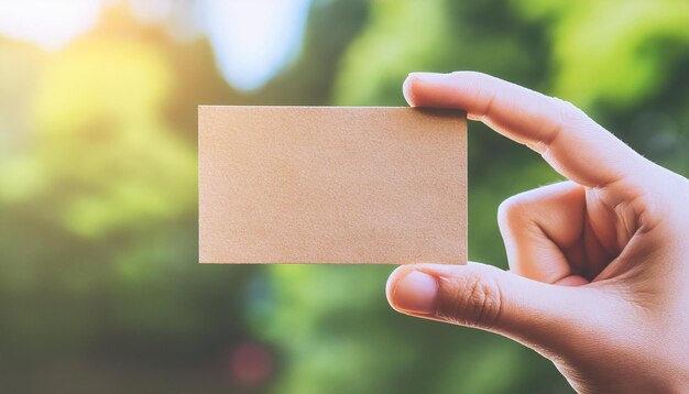 Hand holding mockup of empty kraft business card blurred natural background Branding presentation