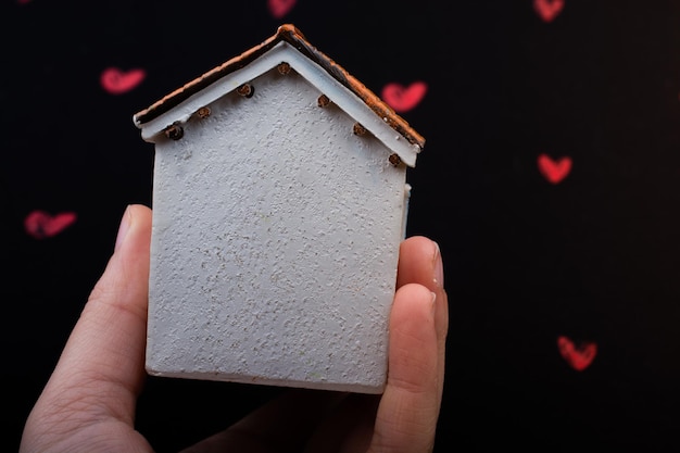 Hand holding a model house on background with red hearts